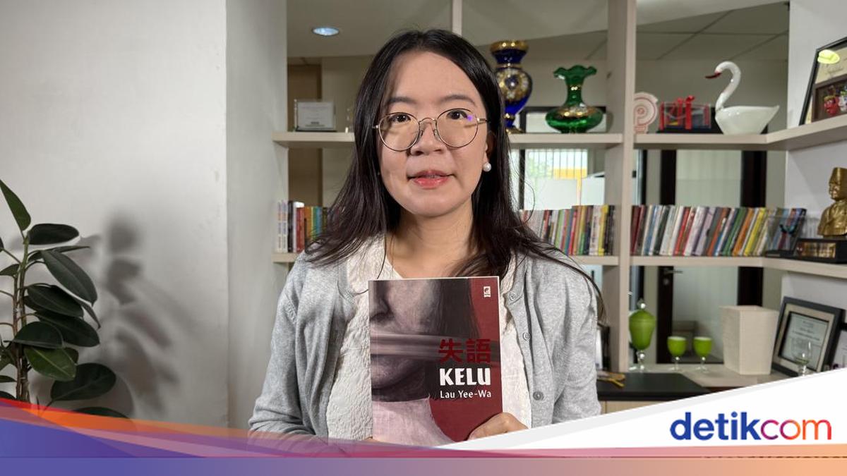 本棚を背に小説『Kelu』を手にする香港の作家ラウ・イーワ