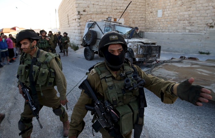 An Israeli soldier gestures during confrontations with Palestinians in Qafr Malik village near the West Bank city of Ramallah June 14, 2015. An Israeli army jeep struck and killed a Palestinian in the occupied West Bank on Sunday, with the military and locals giving conflicting accounts of the circumstances. A military spokeswoman said the jeep, which was in Qafr Malik village as part of an operation to arrest suspected militants, accidentally hit the Palestinian after he threw a petrol bomb at it. Local resident Nail Abdul Latah el Hajj denied the Palestinian had attacked the jeep, however, saying the man was walking to work at a chicken farm when he was run down on the main street and then crushed as the vehicle crashed into a wall and overturned. REUTERS/Mohamad Torokman