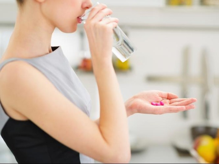 Ilustrasi seorang wanita yang sedang mengonsumsi vitamin atau suplemen