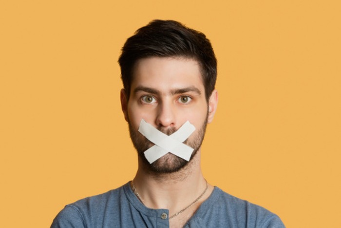 Portrait of a young man with tape on mouth over colored background
