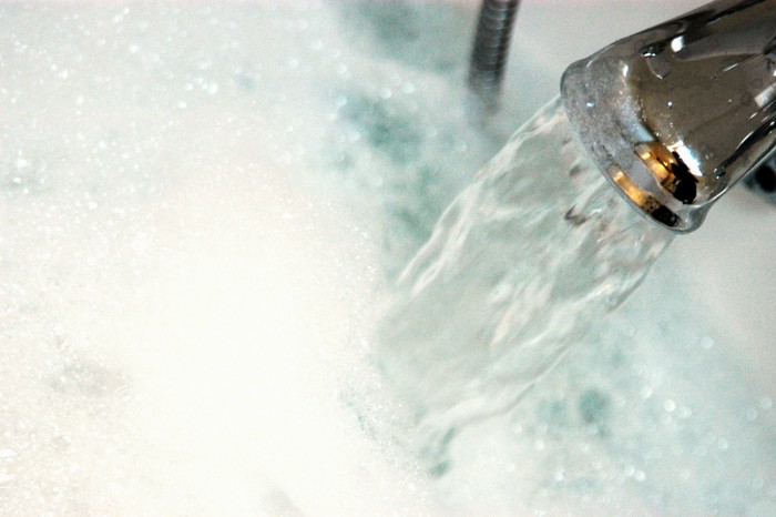 Ilustrasi bak mandi Water gushing from tap into bath containing bubble bath