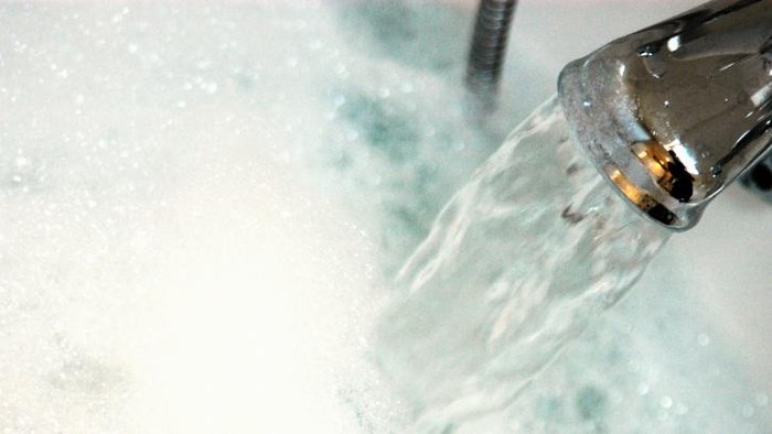 Water gushing from tap into bath containing bubble bath