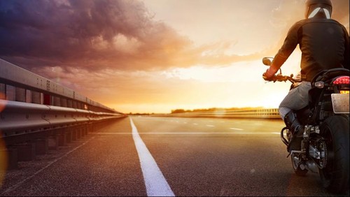 Biker riding motorcycle on an empty road at sunset
