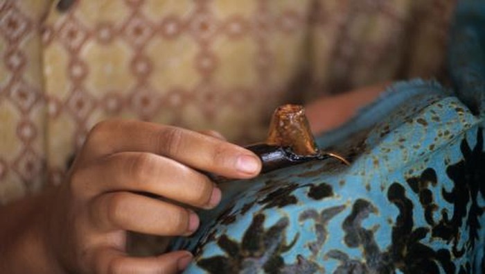 Membatik dengan menggunakan canting dan lilin.