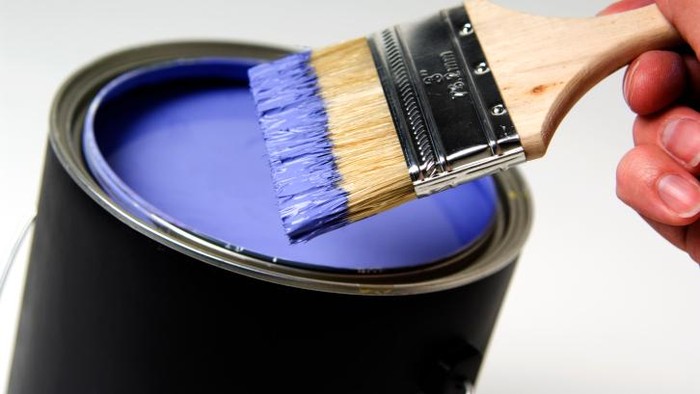 Man dipping paintbrush into purple paint can