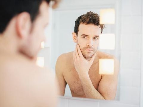 Young man checking his face in bathroom mirror