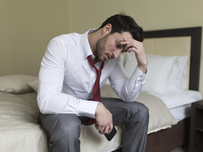 ilustrasi pria sedih Color portrait of a young man in a shirt and black tie, upset, hands on his face, against plain studio background.
