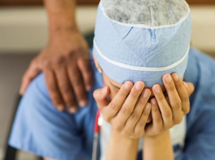 Asian surgeon sitting with head in hands