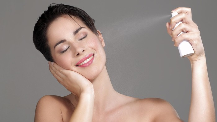 Beautiful woman applying spray water on face