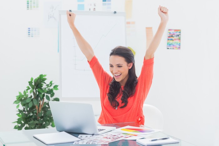 Ilustrasi Wanita semangat bekerja Excited woman raising her arms while working on her laptop