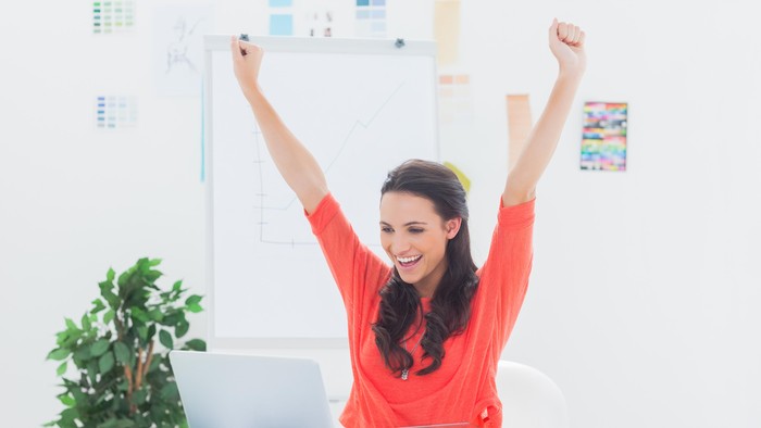 Excited woman raising her arms while working on her laptop
