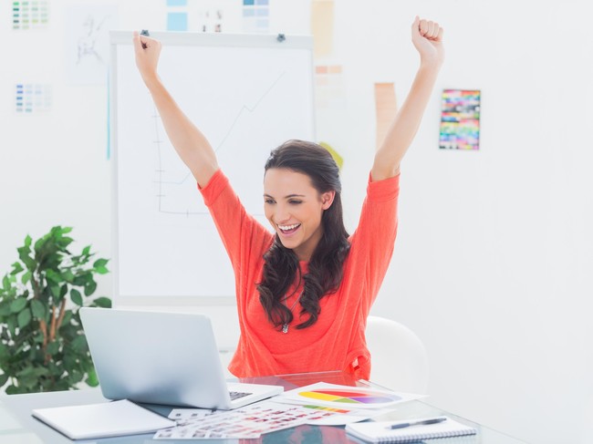 Excited woman raising her arms while working on her laptop