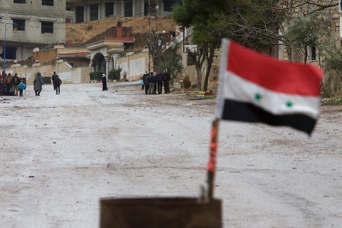 A Syrian national flag flutters near residents who said they have received permission from the Syrian government to leave the besieged town as they wait with their belongings after an aid convoy entered Madaya, Syria, January 14, 2016. Aid was sent on Thursday to the Syrian town blockaded by pro-government forces and two villages besieged by rebels for the second time this week, and a U.N. official said he hoped to make more deliveries to areas where people are starving. Dozens of trucks left Damascus for the town of Madaya at the Lebanese border, and the two villages of Kefraya and al-Foua in rebel-held Idlib province. Tens of thousands of people have been trapped in the areas for months. REUTERS/Omar Sanadiki