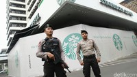 Dua anggota kepolisian tampak berjaga di depan Starbucks yang masih ditutup papan yang mengitari bagian depan cafe tersebut. 