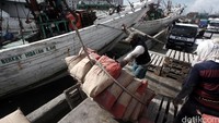 Dua orang pekerja menurunkan semen dari atas kapal.