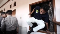 Petugas keluar dari jendela kos usai melakukan penggeledehan.