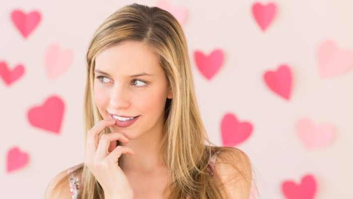 Smiling blonde showing pink heart on the beach