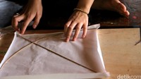 Lalu, ia lekatkan bahan yang akan digunakan sebagai layang-layang, seperti kertas ataupun plastik.