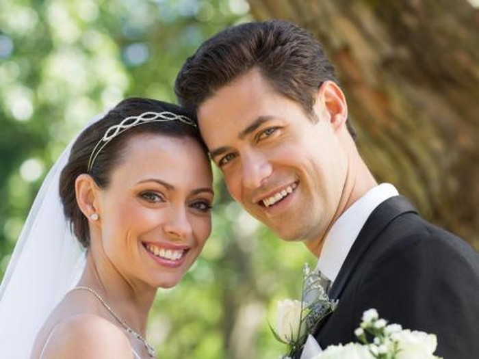 Portrait of the Smiling Bride and Groom Cutting a Wedding a Cake at the Reception