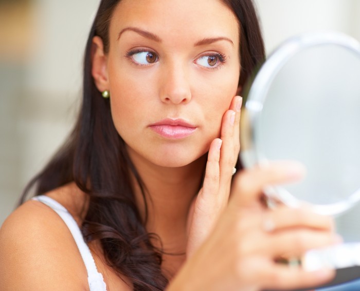 Wanita menyentuh kulit Closeup portrait of young lady holding a mirror