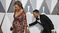John Legend tampak merapikan gaun sang istri, Chrissy Teigen yang berpose di red carpet. REUTERS/Adrees Latif/detikFoto.