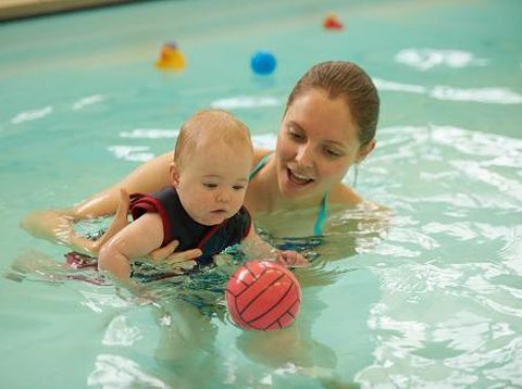 Mother and baby daughter in swimming pool playing with ball