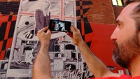 Begitu aplikasi terbuka, Brian mengarahkan kamera ponselnya ke arah mural. Voila! Di layar ponsel, muncul tulisan berwarna biru dan beberapa efek lainnya. Wanita yang digambar masih sama, namun posenya berbeda! (Sastri/detikTravel)