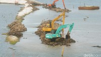 Alat berat bekerja menimbun laut dengan tanah.