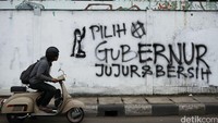 Pengendara sepeda motor melintas di depan mural bertuliskan Pilih Gubernur Jujur dan Bersih di Jakarta, Rabu (30/03/2016).