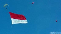 Penerjun meliuk-liuk di udara sambil membawa bendera merah putih raksasa.