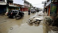 Pengendara melintas di jalan yang diselimuti lumpur.