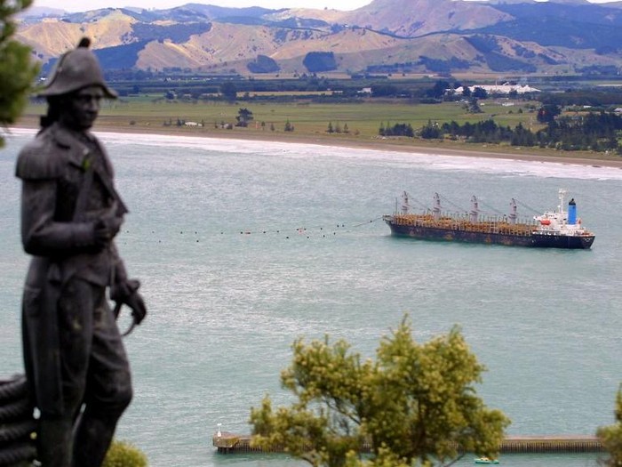 A statue of British explorer Captain James Cook overlooks the grounded South Korean log carrier Jody F Millennium at Gisborne on the North Island, 13 February 2002 as fears mount that it may break up and spill 650 tonnes of heavy oil fuel.  Ocean-going tugs are preparing to pull the 156-metre Panamanian registered bulk carrier off the sand ahead of forecast severe weather conditions. The ship became stuck fast on the beach that acquired world-wide fame during Millennium celebrations, as Gisborne was the first city to see the light of the new century, after being battered by a storm and huge swells on 06 February.  AFP PHOTO/Dean TREML / AFP PHOTO / DEAN TREML