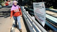 Seorang warga melintas di depan spanduk pengumuman larangan membuang sampah ke dalam sungai.