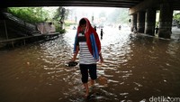 Seorang warga melintas di jalan yang terendam banjir.