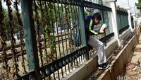 Seorang siswa menyeberangi perlintasan KA dengan mencari celah yang lebih besar pada pagar yang menutup rel.