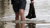 Seorang warga berjalan menembus banjir dengan menenteng sepatu. REUTERS/Christian Hartmann.