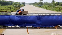 Tiga orang pekerja memindahkan beton dari atas jembatan yang masih dalam tahap pengerjaan.