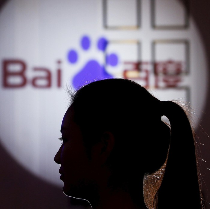 A woman is silhouetted against the Baidu logo at a new product launch from Baidu, in Shanghai, China, November 26, 2015. REUTERS/Aly Song/File Photo