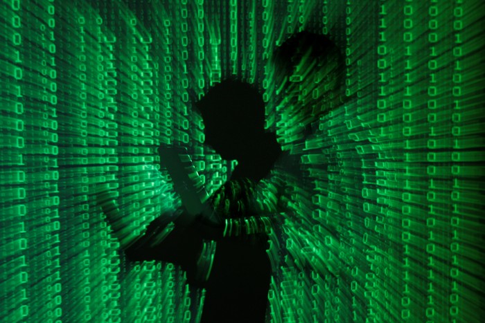 Reaktualisasi Ketahanan Nasional melalui Geo-Cybernetics Ilustrasi mengenai ancaman cyber dalam konteks ketahanan nasional melalui Geo-Cybernetics, menunjukkan seorang pria dengan laptop dan kode biner