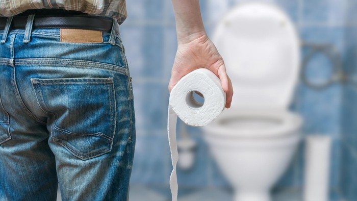 Man suffers from diarrhea holds toilet paper roll in front of toilet bowl.