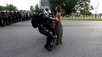 Foto yang disebut sebagai simbol aksi protes terhadap kebrutalan polisi AS itu, menunjukkan seorang wanita kulit hitam dengan gaun panjang tengah berdiri tenang di tengah jalan, tanpa reaksi wajah berlebihan, di hadapan dua polisi yang menangkapnya. Jonathan Bachman/Reuters/detikFoto.