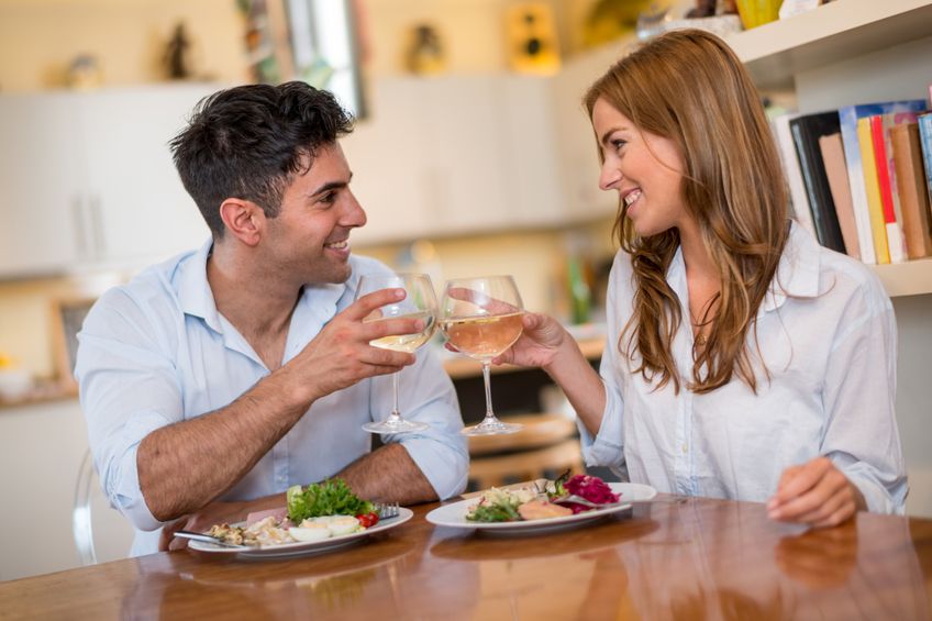 Photo of romantic dinner in expensive hotel. Young couple smiling while having dinner. Girl treating and feeding her boyfriend with salad