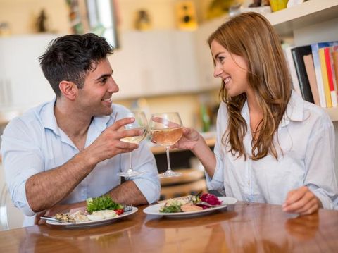 Photo of romantic dinner in expensive hotel. Young couple smiling while having dinner. Girl treating and feeding her boyfriend with salad