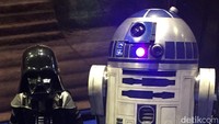 Seorang anak yang memakai kostum Darth Vader dan berpose di sebelah R2-D2.