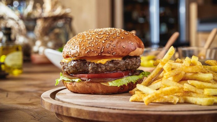 junk food A man holding a fresh hamburger and second one waiting in row. Fresh ground burger with onion, lettuce, tomato served with french fries.
