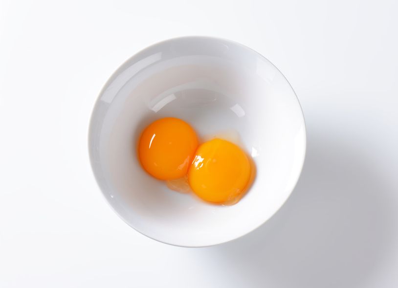 two raw egg yolks in white bowl on white background