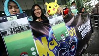 Mereka membawa spanduk dan boneka pokemon.