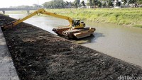 Petugas dengan alat berat mengangkat sampah dan lumpur yang mengendap di sungai.