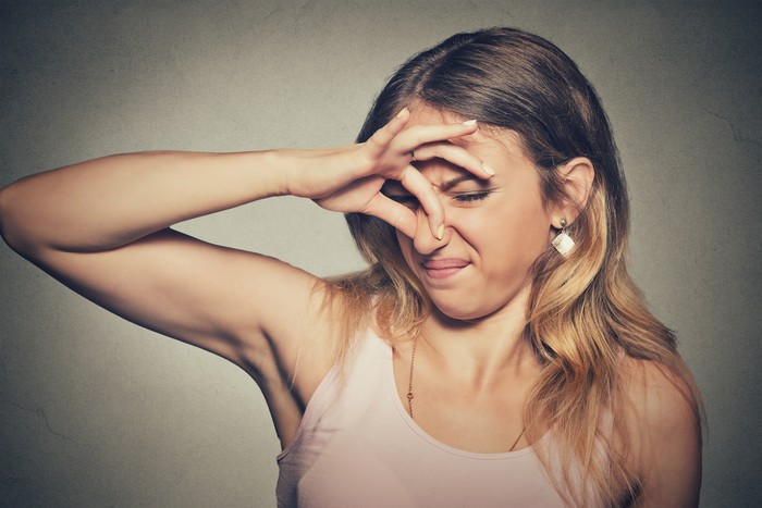 Closeup portrait headshot woman pinches nose with fingers hands looks with disgust something stinks bad smell situation isolated on gray wall background. Human face expression body language reaction