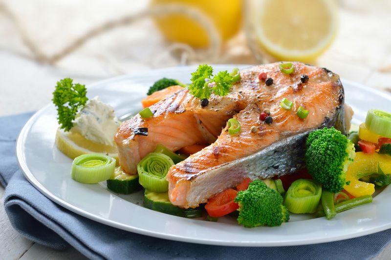Tasty roasted and grilled salmon steak on mixed colorful vegetables, lemons and a fishing net in the background